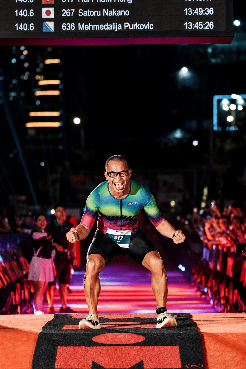 Coach Phạm Hải tại vạch đích Ironman 140.6 Đà Nẵng 2026 — bib #317 — 13:46:28